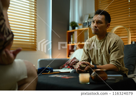 Tarot reader predicting future for young woman visitor in dark room. Forecasting and divination concept 116324079