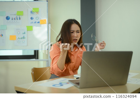 Frustrated female office worker sitting at her desk, staring at her laptop with perplexed expression 116324094