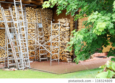 Backyard in summer. Firewood and stepladders of different heights. Organisation of working space. Outside behind house. Backyard in summer. Firewood and stepladders of different heights. Organisation of working space. Outside behind house. 116324809