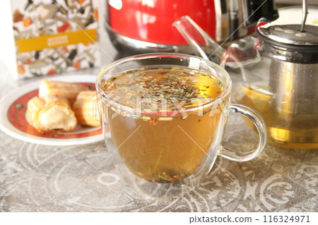 Herbal tea in glass cup. Teapot on table, vanilla eclair pie In kitchen. Herbal tea in glass cup. Teapot on table, vanilla eclair pie In kitchen. 116324971