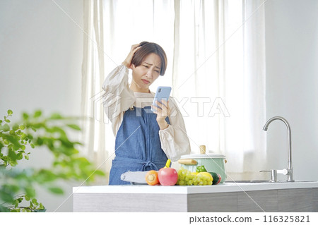 A woman looking at her smartphone while worrying in the kitchen A woman looking at her smartphone while worrying in the kitchen 116325821