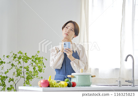 A woman using a smartphone while worrying in the kitchen A woman using a smartphone while worrying in the kitchen 116325823