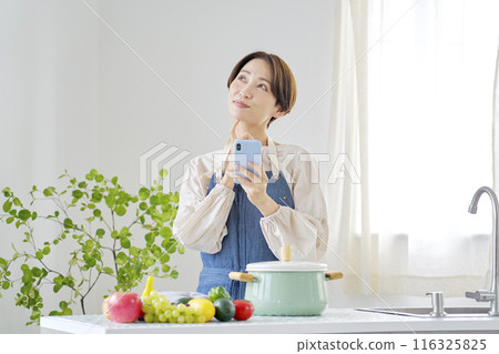 A woman using a smartphone while imagining in the kitchen 116325825