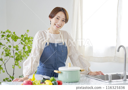 Portrait of a woman standing in the kitchen looking at the camera 116325836