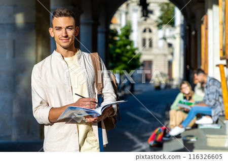 Happy university male student standing at campus with book 116326605