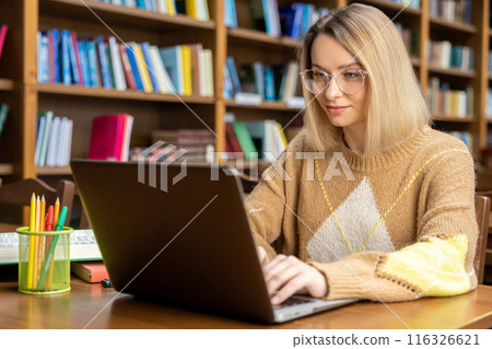Young blonde woman working on a laptop in the library 116326621