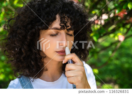 Dark-haired young woman using nasal spray while having allergy symptoms Dark-haired young woman using nasal spray while having allergy symptoms 116326831