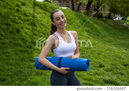 Fit athletic woman with karemat for outdoor yoga exercising 116326897