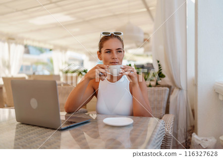 Woman coffee cafe laptop. Coffee break in cafe with sea view . Tranquil long haired woman drinking coffee in plant filled place. Woman sitting at a coffee shop with mobile phone drinking coffee. 116327628