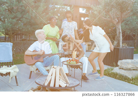 Multiracial group of friends is playing guitar, singing songs at dinner party in summer picnic Multiracial group of friends is playing guitar, singing songs at dinner party in summer picnic 116327866