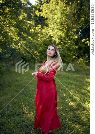 portrait of a beautiful 30-year-old woman with long blond hair in a red dress in a park 116328636