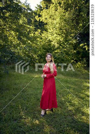 portrait of a beautiful 30-year-old woman with long blond hair in a red dress in a park 116328639