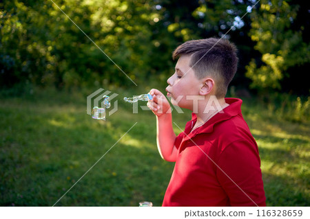 a preteen boy in a red T-shirt catches soap bubbles in the park 116328659