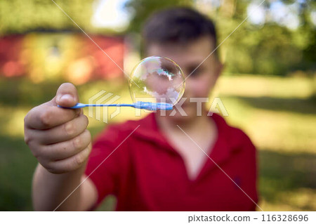 a preteen boy in a red T-shirt catches soap bubbles in the park 116328696