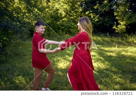 mother and preteen son in red clothes are circling and running in the garden mother and preteen son in red clothes are circling and running in the garden 116328721