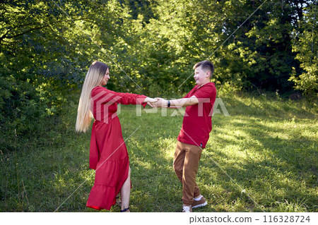 mother and preteen son in red clothes are circling and running in the garden mother and preteen son in red clothes are circling and running in the garden 116328724