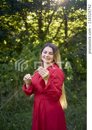 portrait of a beautiful 30-year-old woman with long blond hair in a red dress in a park 116328742