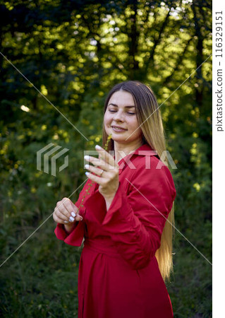 portrait of a beautiful 30-year-old woman with long blond hair in a red dress in a park 116329151