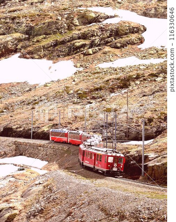 The red train of the Rhaetian Railway Bernina Line runs through an S-shaped curve along the "White Lake" (Lago Bianco). 116330646