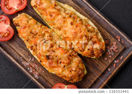 Zucchini halves baked with cheese, tomatoes, meat or meat substitute 116331441