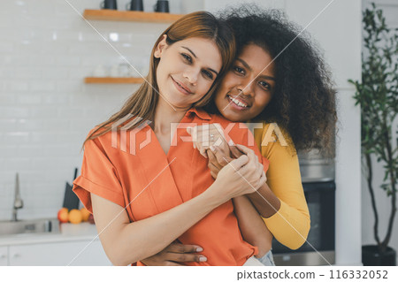 Multiethnic lesbian couple having embracing in kitchen room 116332052