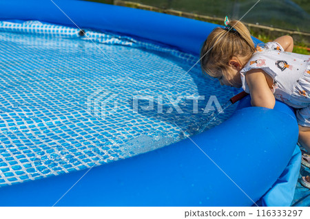 A child pours water from a hose into the pool. On a sunny summer day in the backyard, a child fills an inflatable pool with cold water from a hose. On a hot day, fill the inflatable pool with water. A child pours water from a hose into the pool. On a sunny summer day in the backyard, a child fills an inflatable pool with cold water from a hose. On a hot day, fill the inflatable pool with water. 116333297