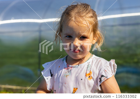 A cute child with a wet face stands in the garden and smiles at the camera. Portrait of a child with drops of water on his face on a hot summer day. A beautiful child with a wet face outside. A cute child with a wet face stands in the garden and smiles at the camera. Portrait of a child with drops of water on his face on a hot summer day. A beautiful child with a wet face outside. 116333302