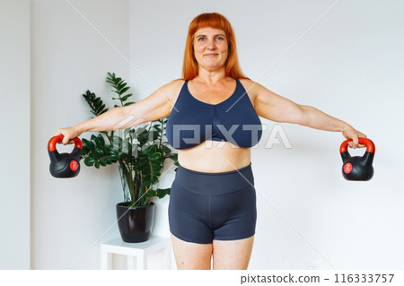 portrait red-haired middle-aged woman, plump, with large bust size, doing fitness at home 116333757