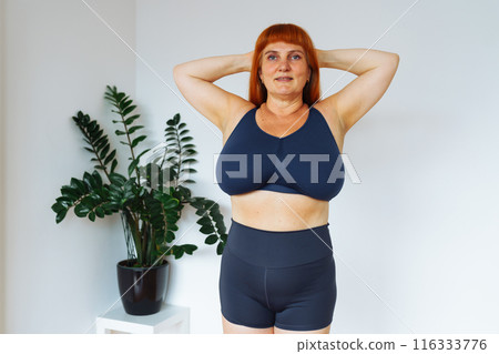portrait red-haired middle-aged woman, plump, with large bust size, doing fitness at home 116333776