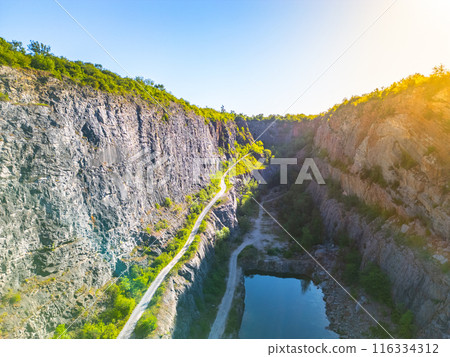 Elevated perspective of the abandoned Velka Amerika limestone quarry, featuring towering cliffs, sparse vegetation, and a reflective pond at sunset. Morina, Czechia Elevated perspective of the abandoned Velka Amerika limestone quarry, featuring towering cliffs, sparse vegetation, and a reflective pond at sunset. Morina, Czechia 116334312