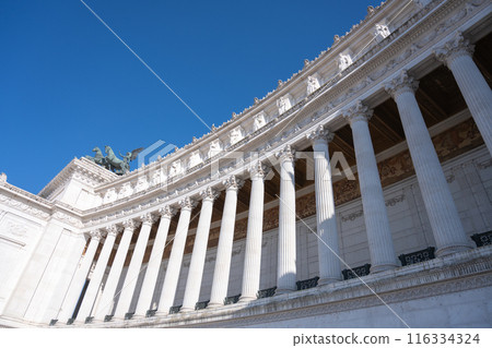 A low-angle view of the Vittoriano in Rome, showcasing its intricate white marble columns and decorative architectural details. Rome, Italy A low-angle view of the Vittoriano in Rome, showcasing its intricate white marble columns and decorative architectural details. Rome, Italy 116334324