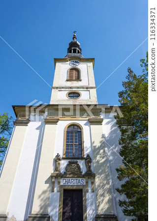 A low-angle view of Saint Lawrence Church in Potstejn, Czechia, showcasing the churchs facade, bell tower, and a sign reading Charitas. A low-angle view of Saint Lawrence Church in Potstejn, Czechia, showcasing the churchs facade, bell tower, and a sign reading Charitas. 116334371
