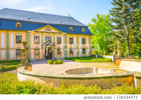Charming small baroque chateau Potstejn in the Czech Republic. The front view includes a fountain and lush green surroundings. Charming small baroque chateau Potstejn in the Czech Republic. The front view includes a fountain and lush green surroundings. 116334372