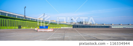 Clear blue skies over the historic Berlin Tempelhof Airport in Germany, showcasing the vast airport tarmac and iconic terminal building with hangars. 116334944