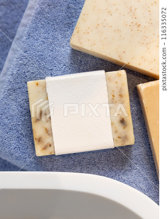 Soap bar with blank label on blue towels near vessel sink in bathroom, packaging mockup 116335072