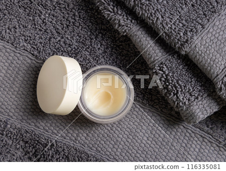Opened lip balm jar with blank lid on dark grey bath towel top view, cosmetic mockup 116335081