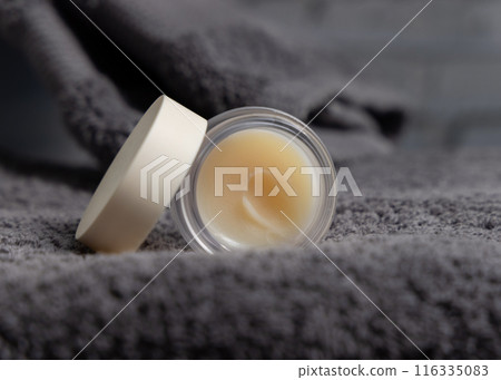 Opened lip balm jar with blank lid on dark grey bath towel closeup, cosmetic mockup Opened lip balm jar with blank lid on dark grey bath towel closeup, cosmetic mockup 116335083
