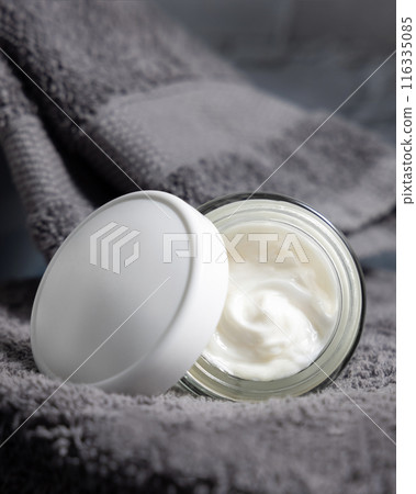 White opened cosmetic jar with white blank lid on grey folded towels in bath, packaging mockup 116335085