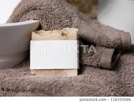Soap bar with blank label on light brown towels near vessel sink in bathroom closeup, mockup 116335086