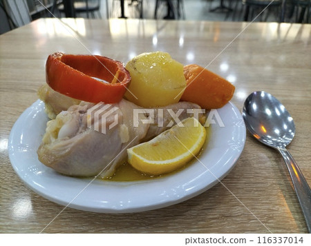 A plate with food in which boiled chicken leg with slices of lemon, potatoes, carrots, red bell peppers in broth. Simple, healthy home-cooked food for life. 116337014