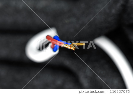 Electrical wires with exposed copper terminals of Insulated white cable in the hand of an electrician wearing black protective gloves closeup 116337075