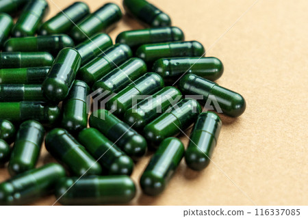 Green herbal health capsules scattered on a light brown surface close up. Naturopathy pills 116337085