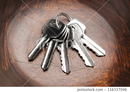A bunch of metal keys to the apartment door lies in a wooden bowl in close up 116337096