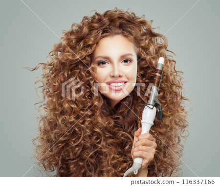Cute young smiling woman holding using hot curling tongs iron on white background. Coiffure Cute young smiling woman holding using hot curling tongs iron on white background. Coiffure 116337166