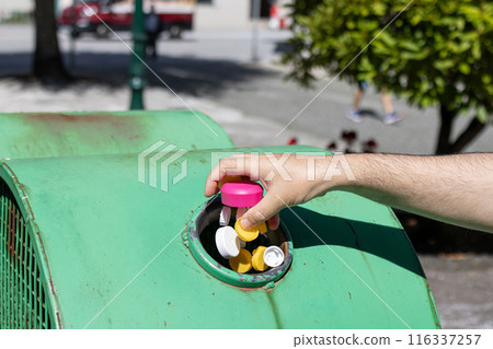 Male Hand throwing plastic bottle caps into an urban recycling bin. Recycle and reuse concept for an environmentally and globally friendly approach Male Hand throwing plastic bottle caps into an urban recycling bin. Recycle and reuse concept for an environmentally and globally friendly approach 116337257