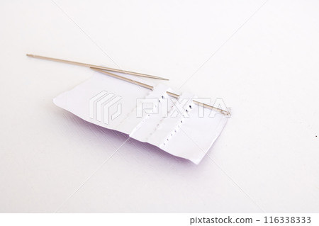 Two sewing needles placed on top of a sheet of paper Two sewing needles placed on top of a sheet of paper 116338333