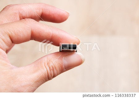 A person is delicately holding a small USB device between their fingers 116338337