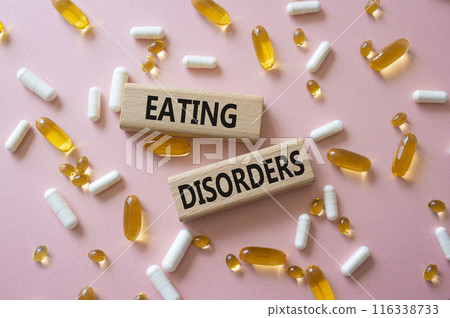 Eating Disorders symbol. Concept word. Eating Disorders on wooden blocks. Beautiful pink background with pills. Medicine and Eating Disorders concept. Copy space 116338733
