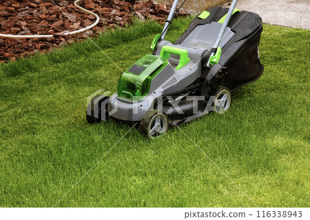 A young man is mowing a lawn with a lawn mower in his beautiful green floral summer garden A young man is mowing a lawn with a lawn mower in his beautiful green floral summer garden 116338943