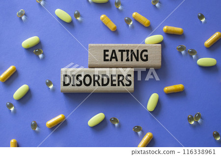 Eating Disorders symbol. Concept word. Eating Disorders on wooden blocks. Beautiful purple background with pills. Medicine and Eating Disorders concept. Copy space Eating Disorders symbol. Concept word. Eating Disorders on wooden blocks. Beautiful purple background with pills. Medicine and Eating Disorders concept. Copy space 116338961